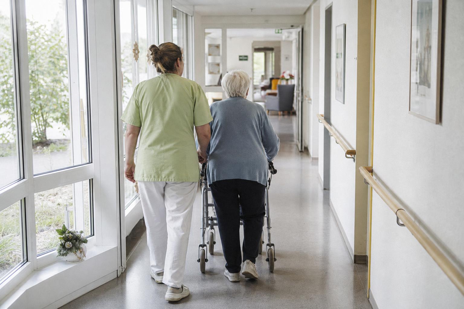 Pflegerin begleitet Bewohnerin mit Rollator durch hellen Heimflur